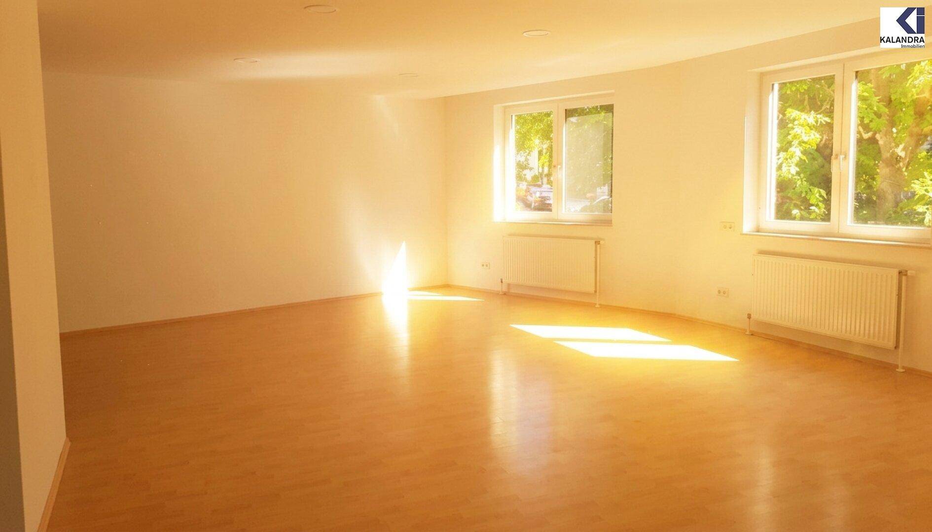 Lichtdurchfluteter Wohnraum mit Parkettboden und großen Fenstern, die viel Helligkeit spenden.