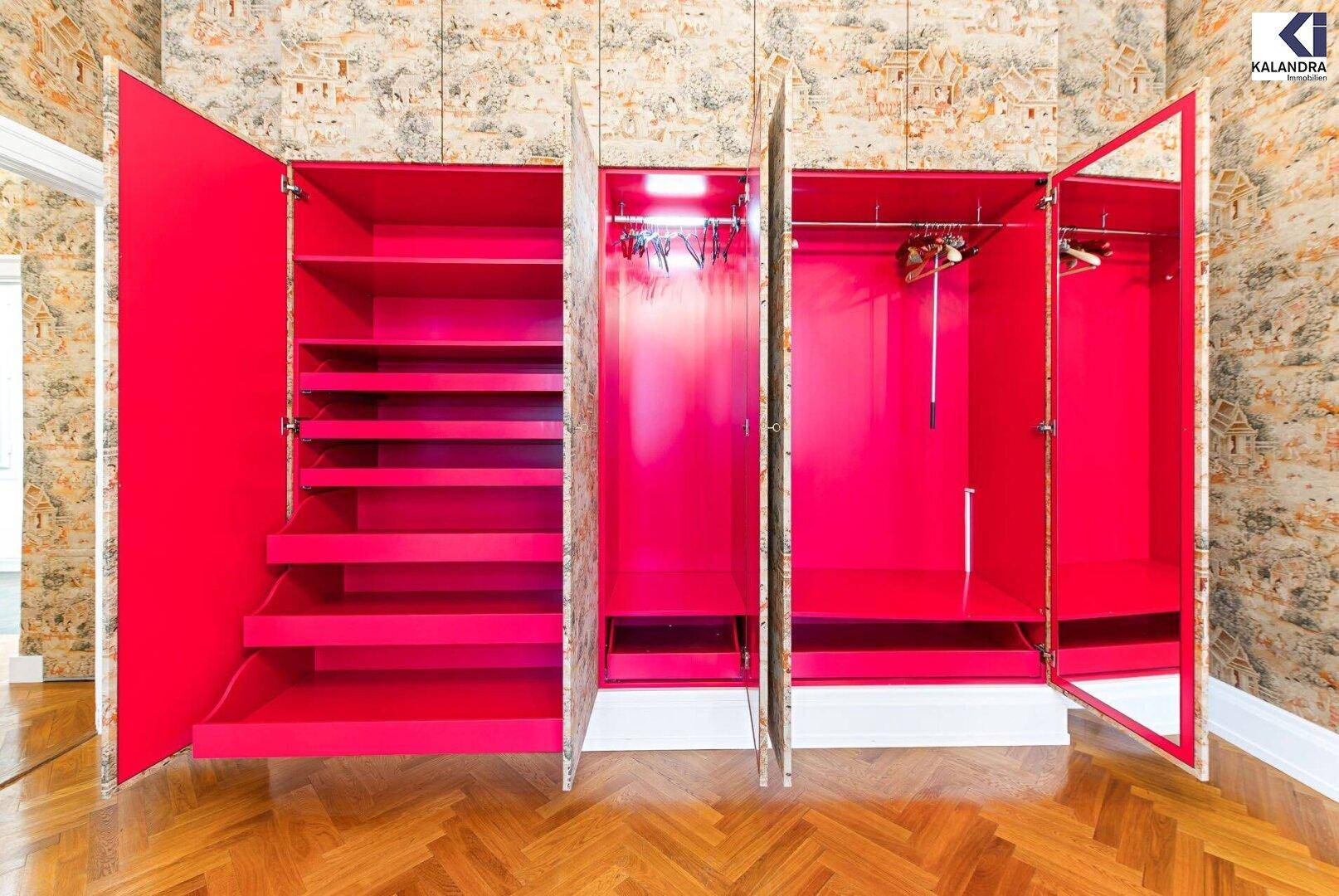 Zimmer mit hellem Fischgrätparkett und einem großen, geöffneten Einbauschrank in leuchtendem Pink.