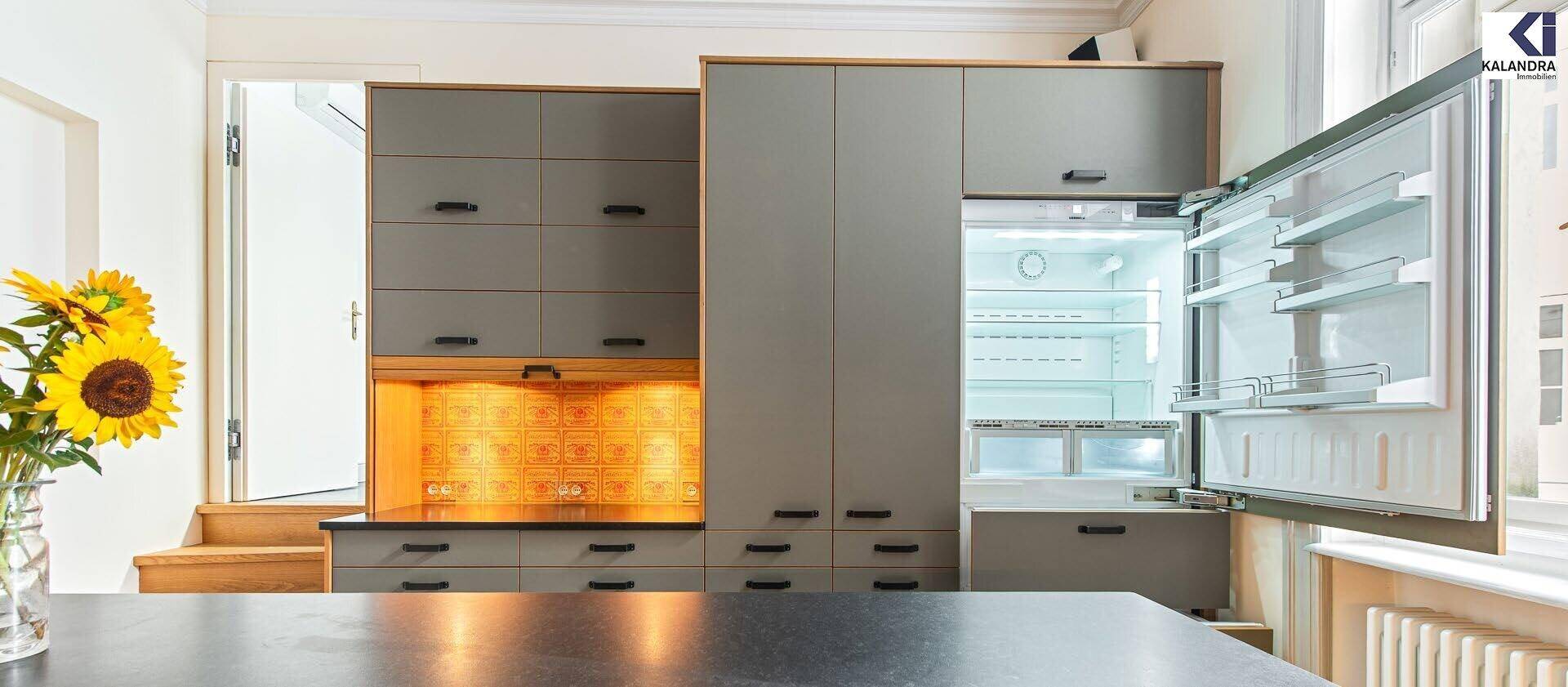 Moderne Küche mit integriertem Kühlschrank, grauen Schränken und gelber Rückwand.