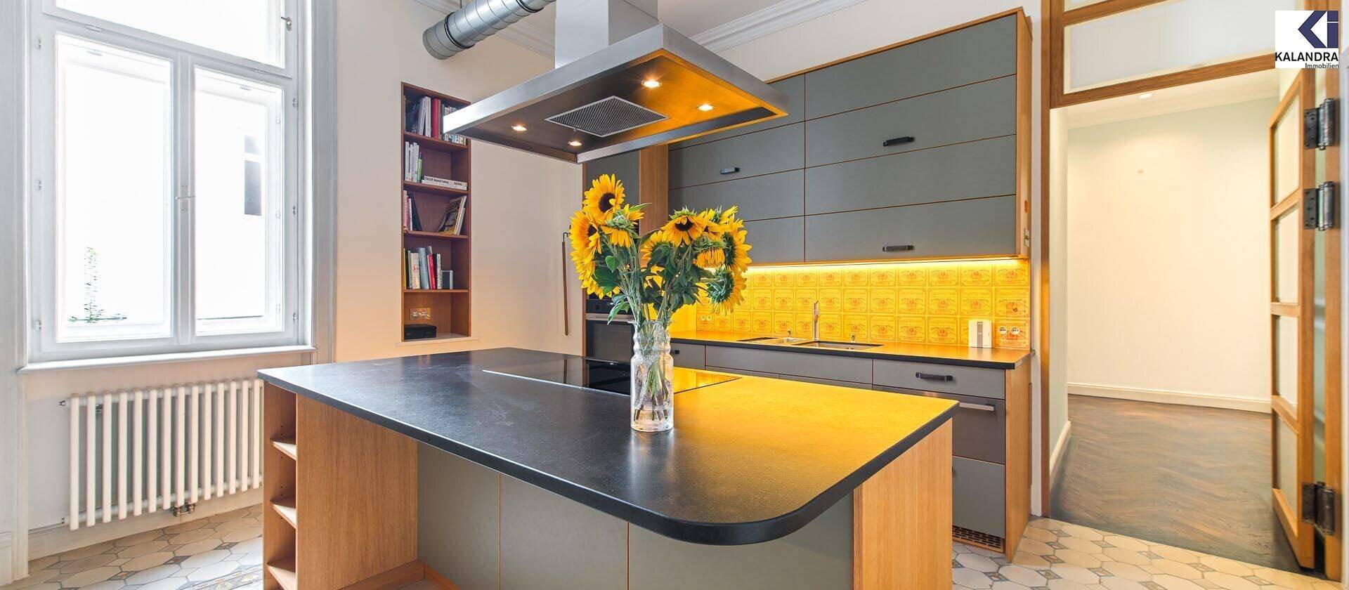 Moderne Küche mit Kücheninsel, grauen Schränken und gelber Rückwand, offen zum Essbereich.