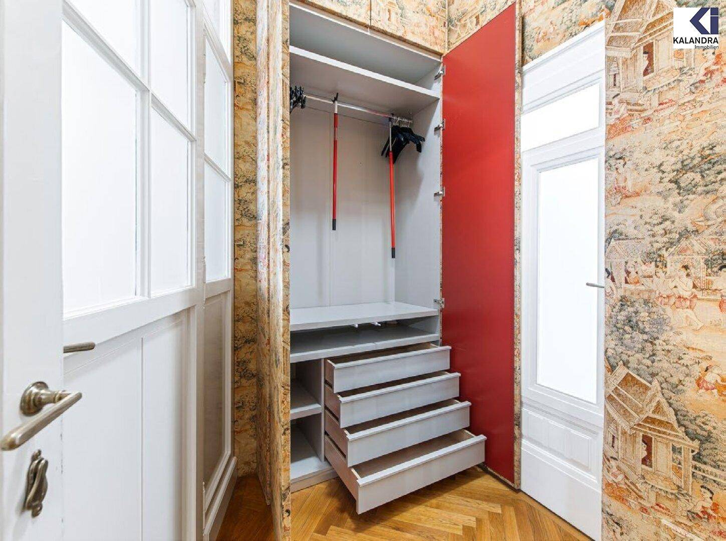 Eingangsbereich mit gemusterter Tapete, hellem Fischgrätparkett und einem geöffneten Einbauschrank.