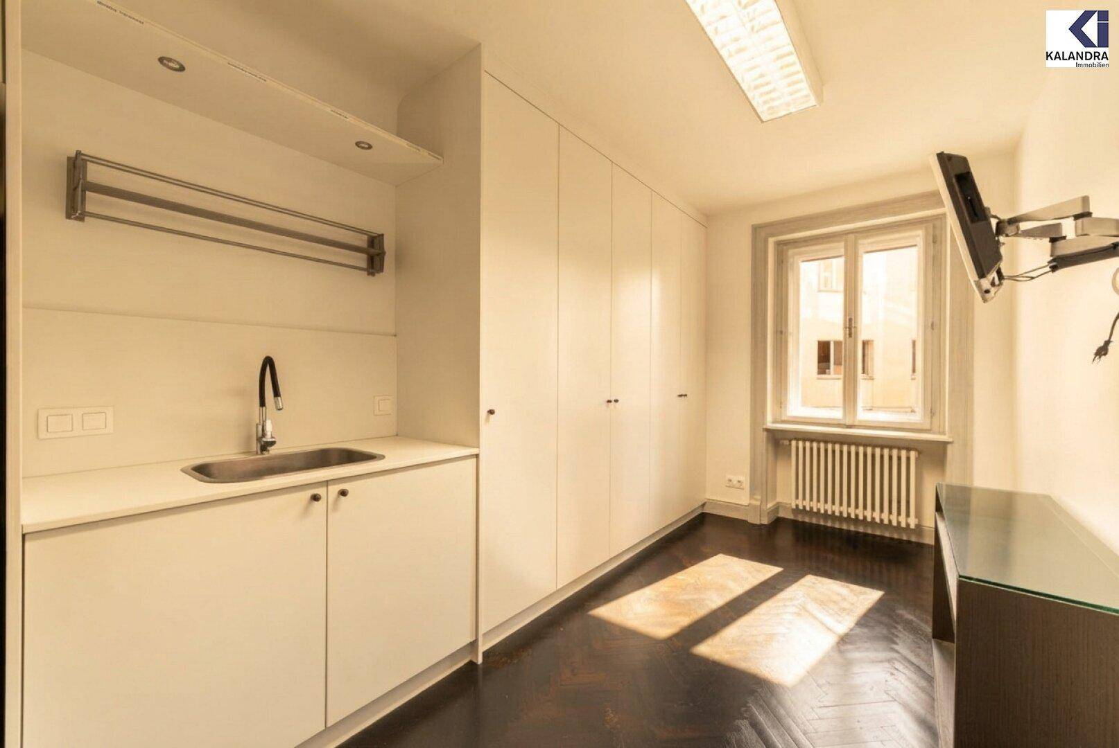Praktischer Hauswirtschaftsraum mit Spülbecken, Einbauschränken und dunklem Fischgrätparkett.