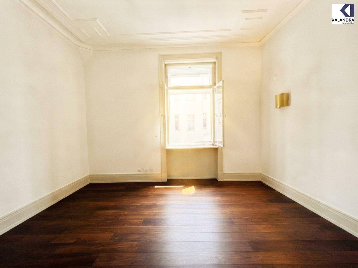 Helles Zimmer mit weißen Wänden, dunklem Holzboden und einem großen Fenster.
