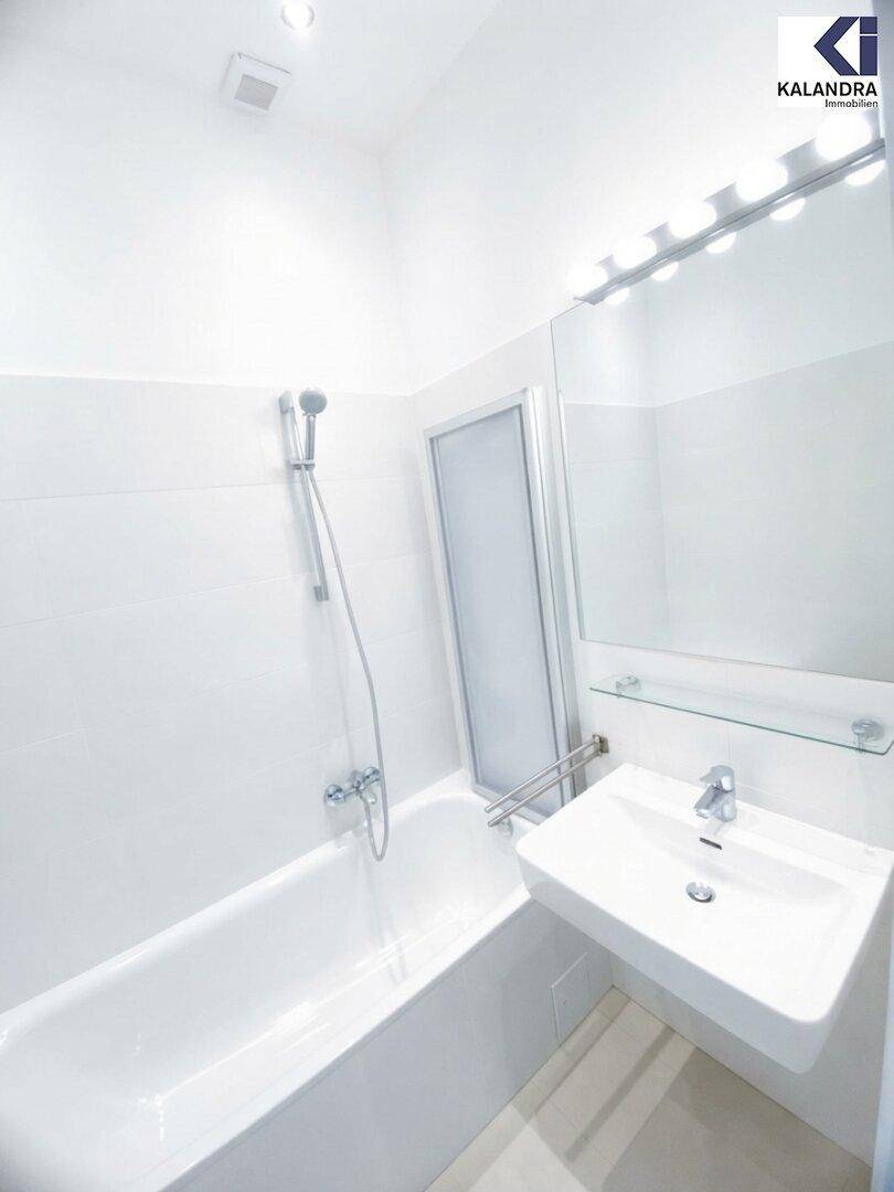 Helles Badezimmer mit Badewanne, Duschvorrichtung, Waschbecken und großem Spiegel, alles in Weiß gehalten.