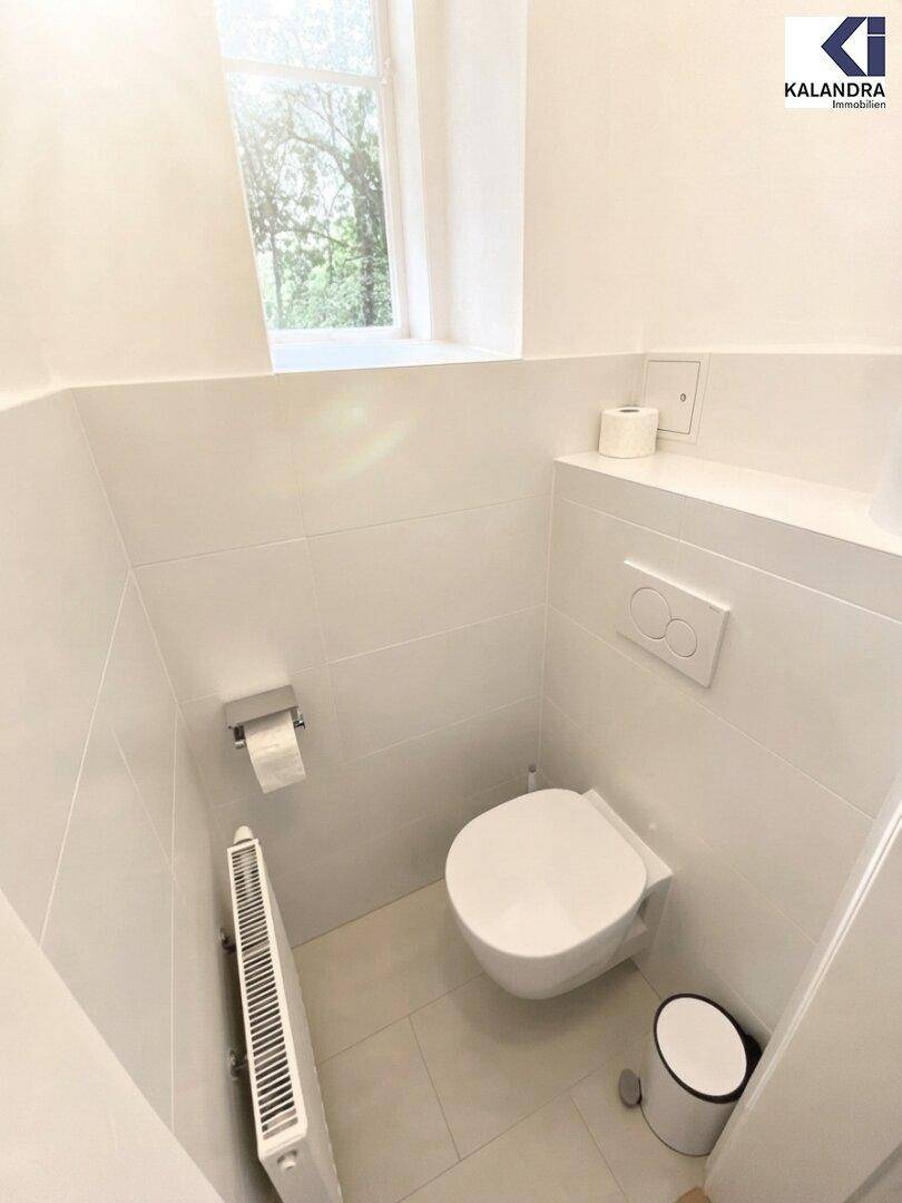 Kleines, helles Gäste-WC mit wandhängender Toilette, Waschbecken und einem Fenster für natürliche Belüftung.