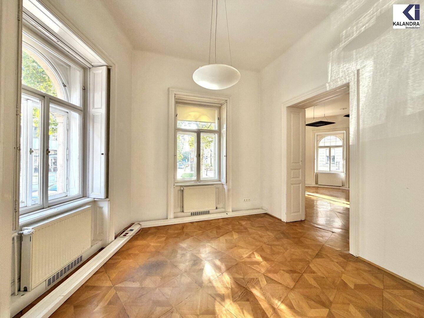 Heller Raum mit Parkettboden, hohen Fenstern und Blick nach draußen, der viel natürliches Licht bietet.