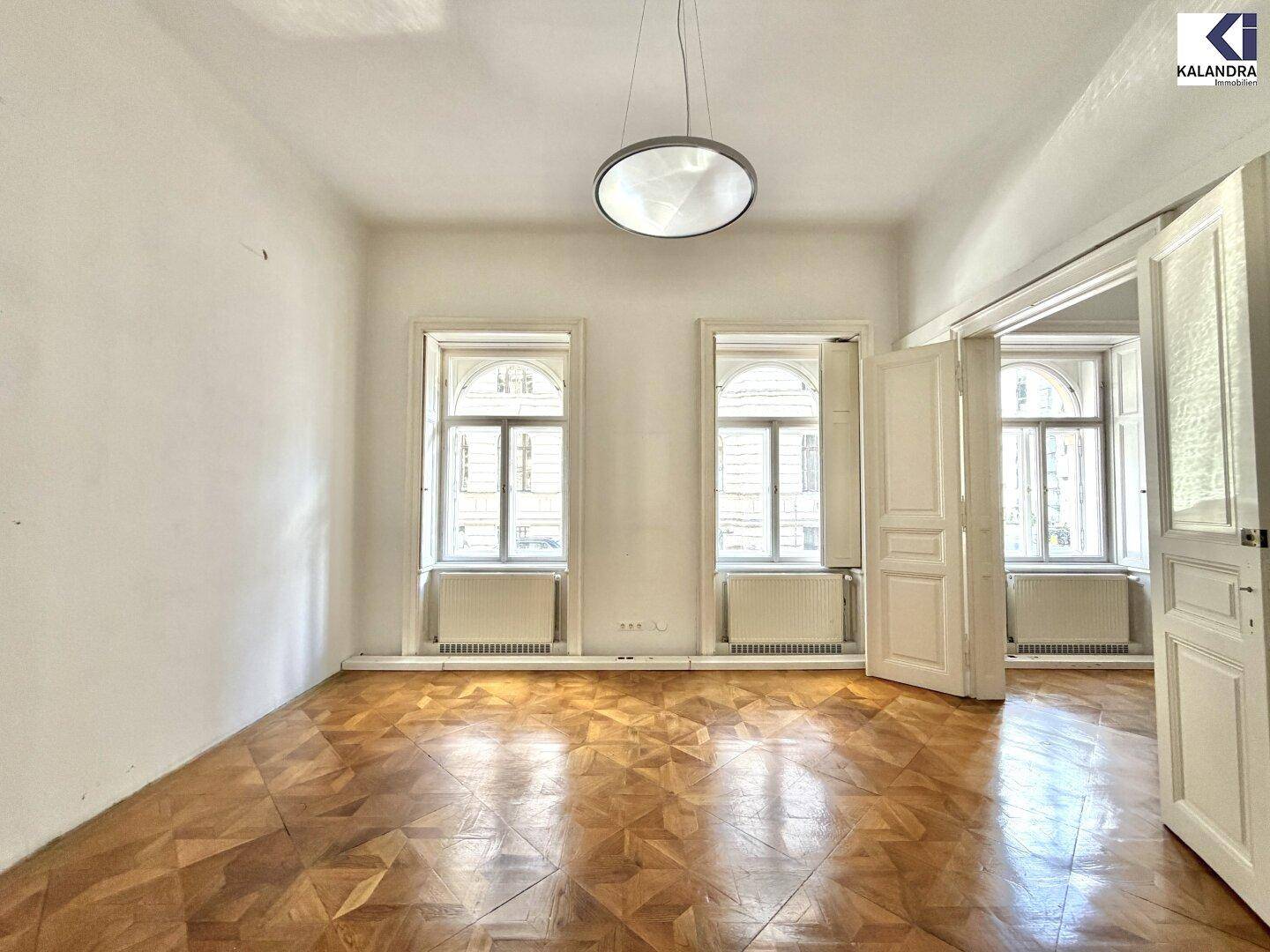 Geräumiges Zimmer mit Parkettboden, hohen Fenstern und viel natürlichem Licht, ideal für Wohnzwecke.