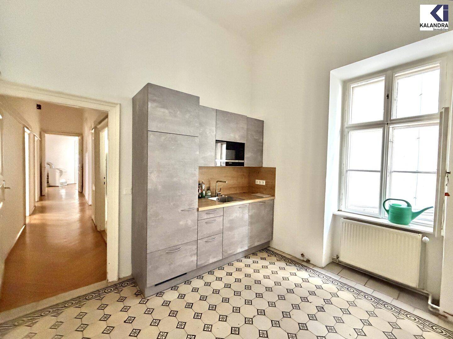 Moderne Küchenzeile mit grauen Schränken, Spüle und Mikrowelle in einem hellen Raum mit Fliesenboden.