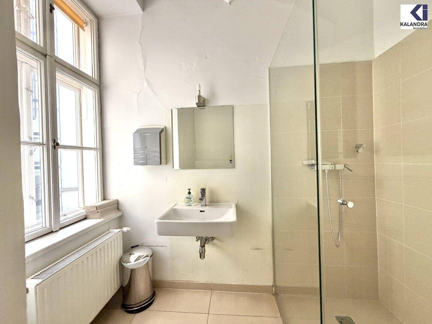 Helles Badezimmer mit Dusche, Waschbecken und Fenster, ausgestattet mit beigen Fliesen und guter Belüftung.
