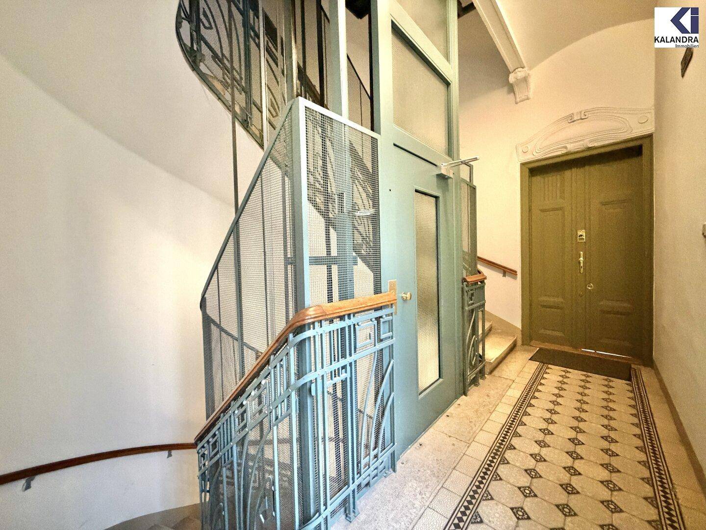Historisches Treppenhaus mit kunstvollem Geländer und modernem Aufzug.