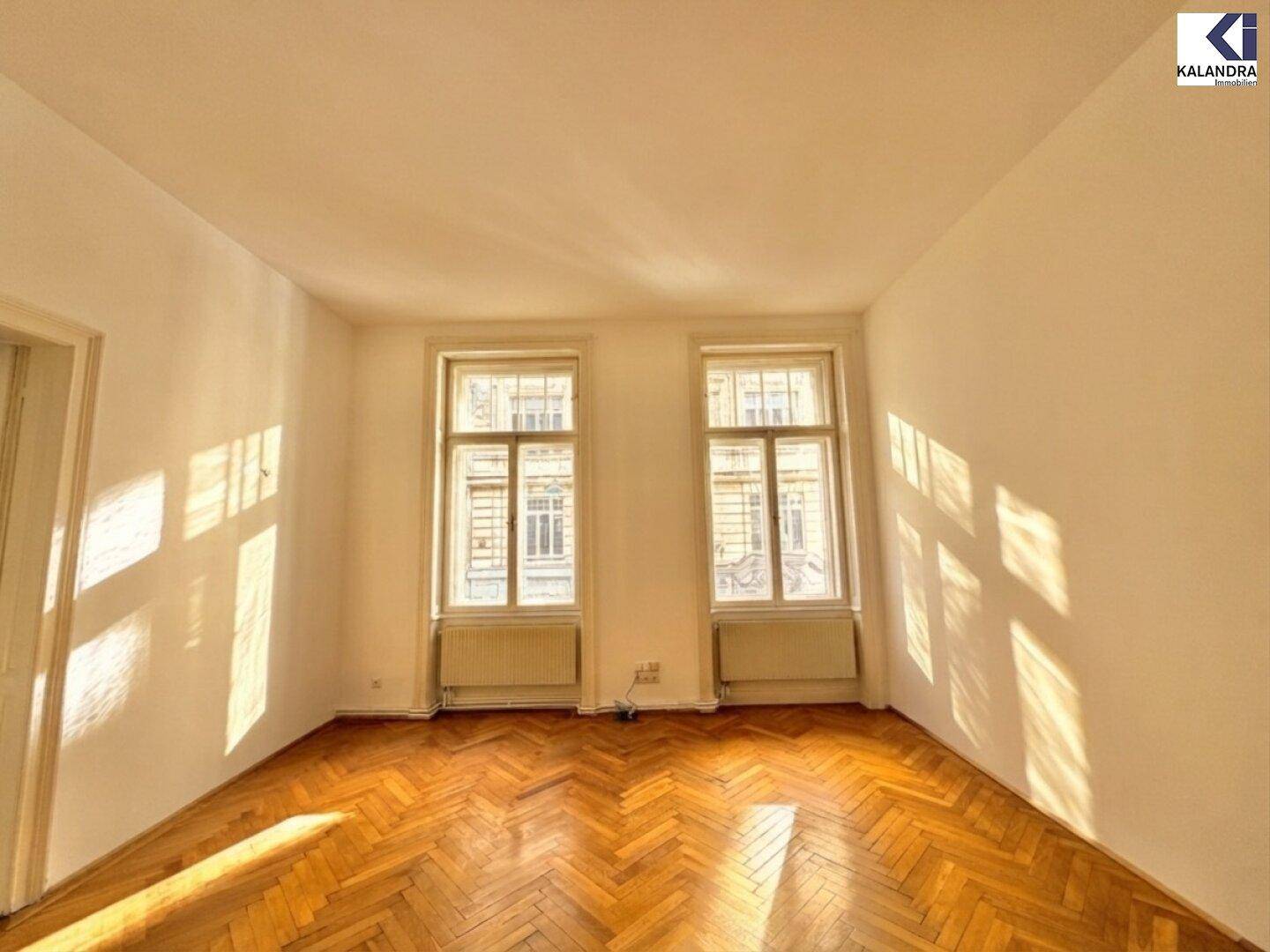 Helles Wohnzimmer mit klassischem Fischgrätparkett und zwei großen Fenstern.
