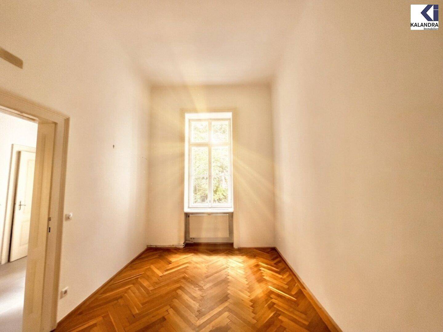 Helles Schlafzimmer mit Fischgrätparkett und einem hohen Fenster, das viel Sonnenlicht bietet.