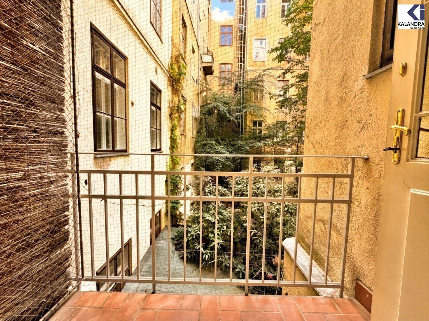 Kleiner Balkon mit Blick auf den begrünten Innenhof eines Altbaus.