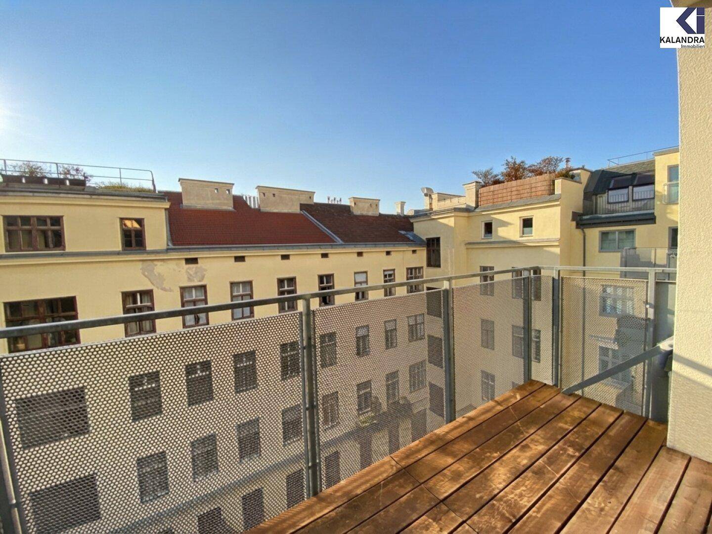 Sonniger Balkon mit Holzboden und Blick auf die umliegenden Gebäude im Innenhof.