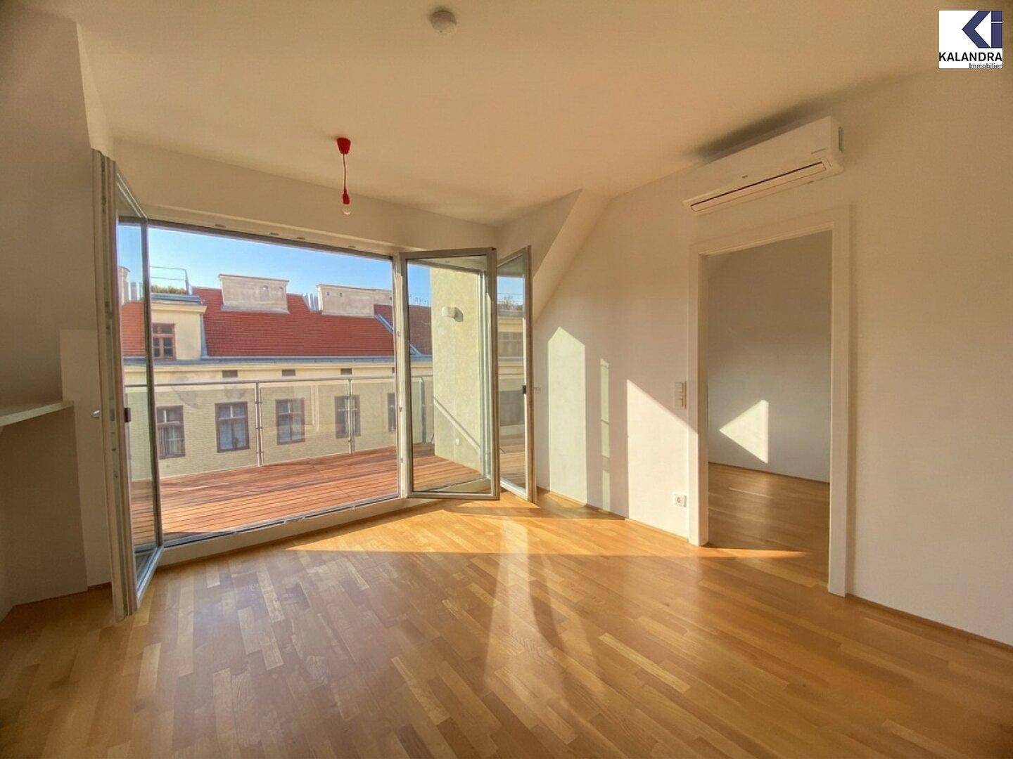 Heller Raum mit Holzboden und weit öffnenden Fenstern zum Balkon, inklusive Klimaanlage.