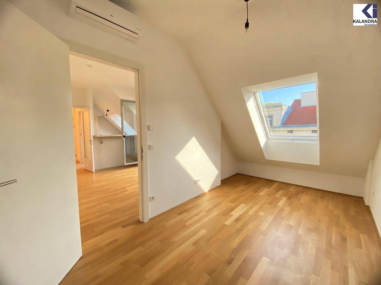Heller Raum mit Holzboden, Dachschräge und Dachfenster, mit Klimaanlage ausgestattet.