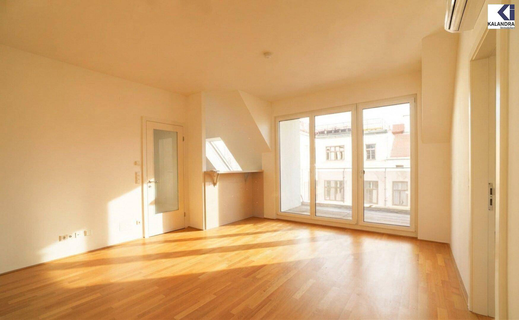 Lichtdurchfluteter Raum mit Holzboden und Zugang zu einem Balkon, ausgestattet mit Klimaanlage.