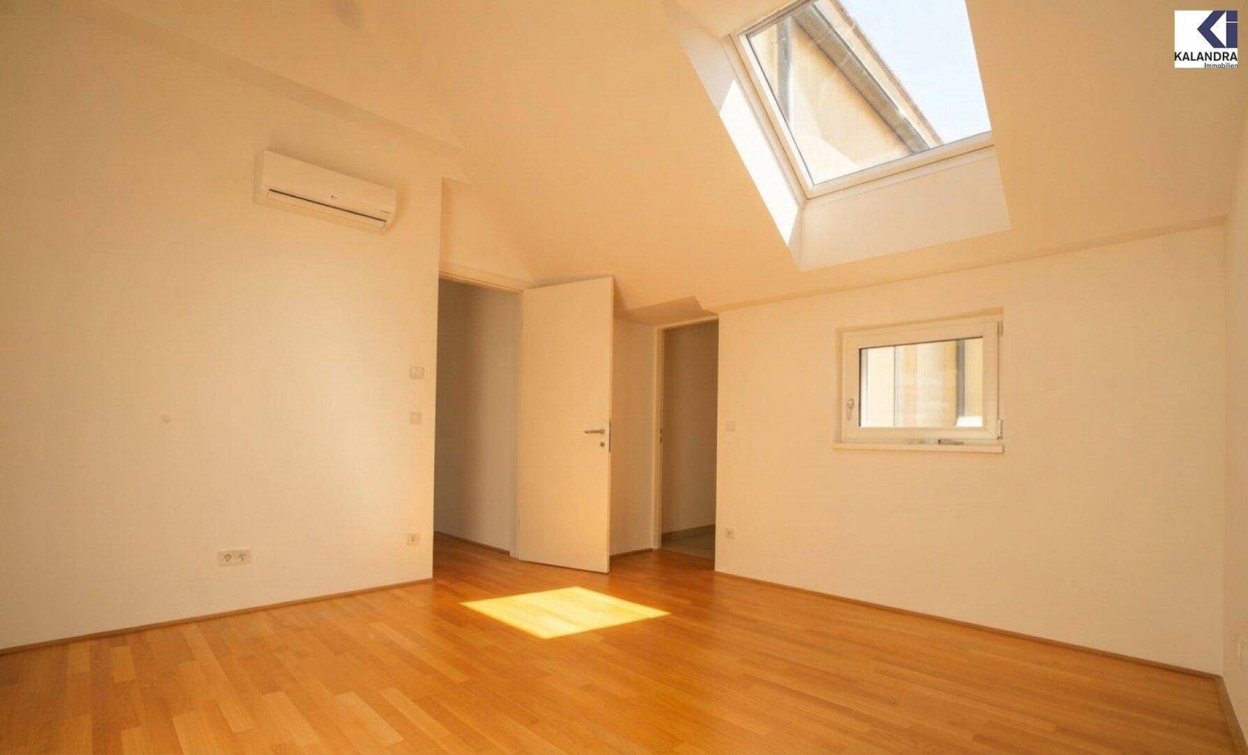 Heller Raum mit Holzboden, Dachschräge und Dachfenster, ausgestattet mit Klimaanlage.