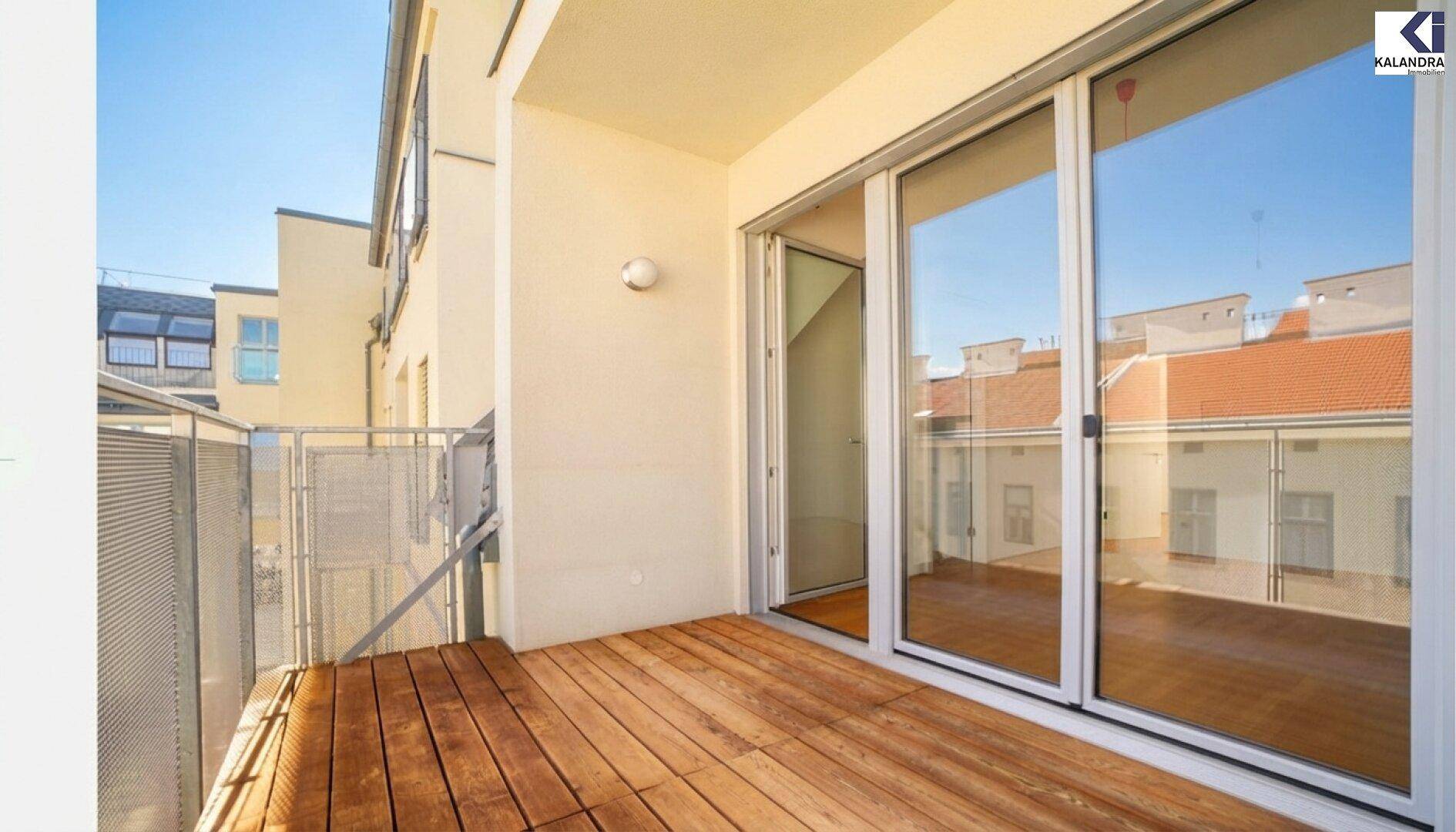 Balkon mit Holzboden und großen Glasschiebetüren, die viel Licht in den Innenraum lassen.