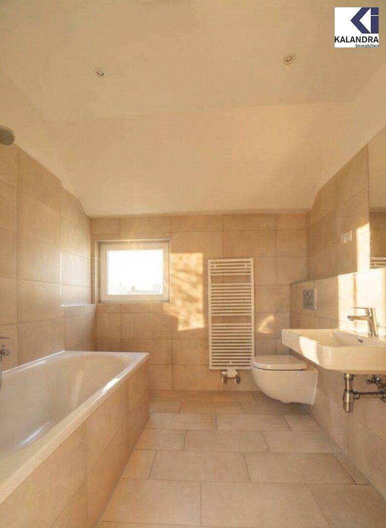 Helles Badezimmer mit Badewanne, WC und Waschbecken, ausgestattet mit Handtuchheizkörper.