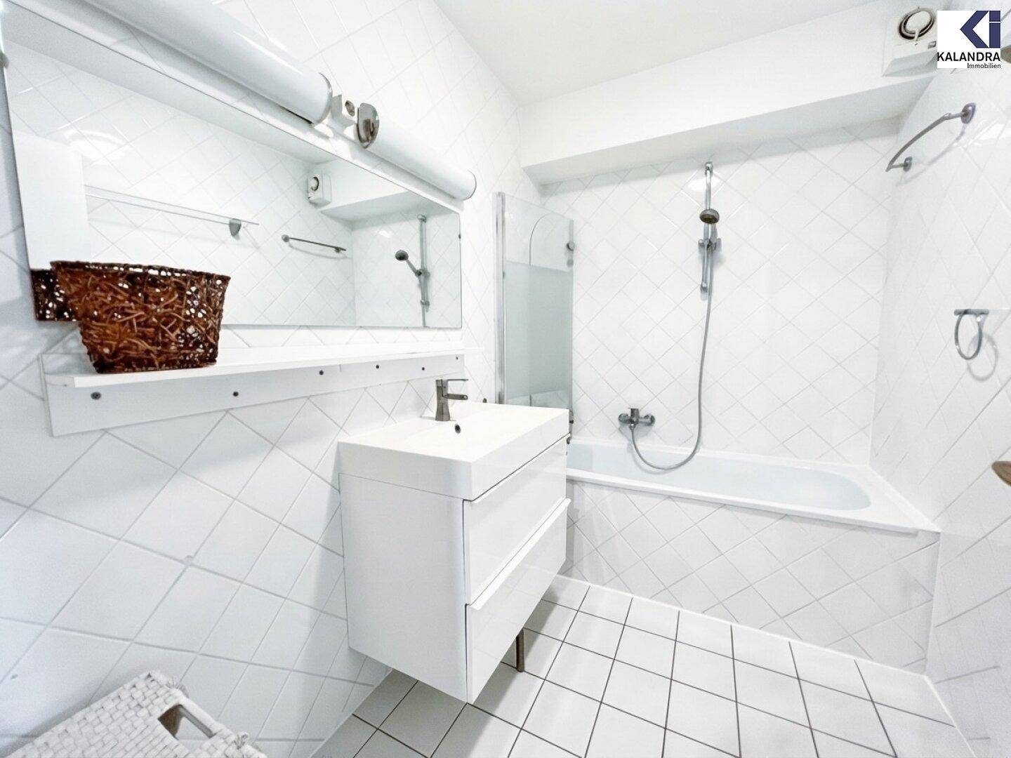 Modernes Badezimmer mit weißen Fliesen, Badewanne und Waschtisch.