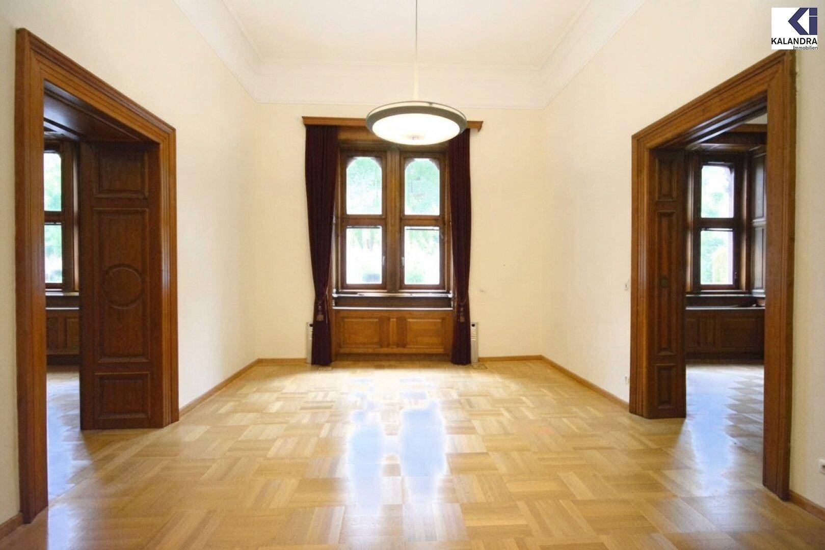 Heller Raum mit Fischgrätparkett, hohen Decken und zwei eleganten Holztüren, die zu weiteren Zimmern führen.