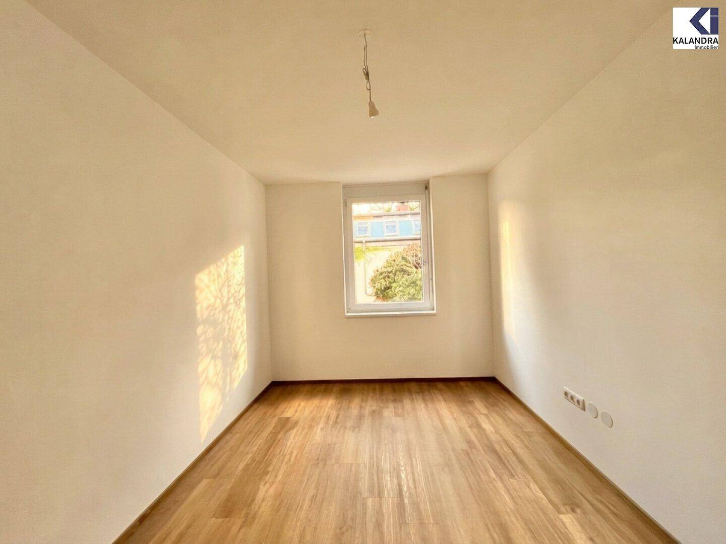 Leeres Zimmer mit Holzboden und einem Fenster, das natürliches Licht in den Raum bringt.