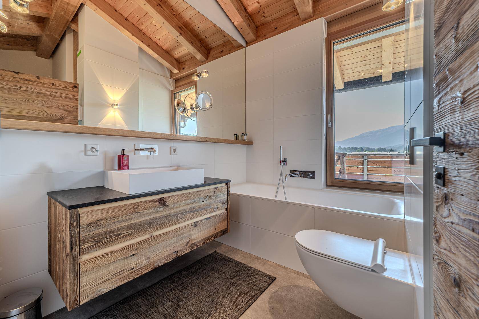 Modernes Badezimmer mit Holzwaschtisch, Badewanne und Fenster mit Bergblick.