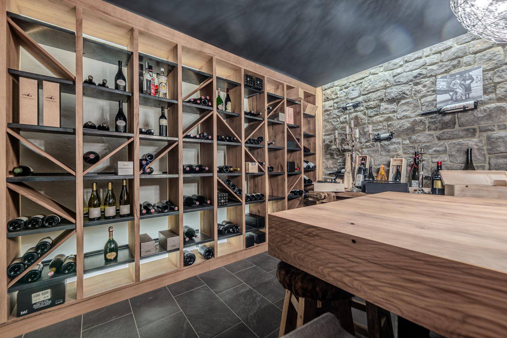 Exklusiver Weinkeller mit umfangreichen Weinregalen, Holztisch und rustikaler Steinwand.