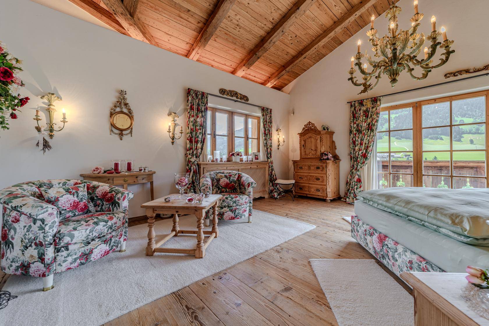 Gemütliches Schlafzimmer mit floralen Sesseln, Holzboden und Zugang zu einem Balkon mit Bergblick.