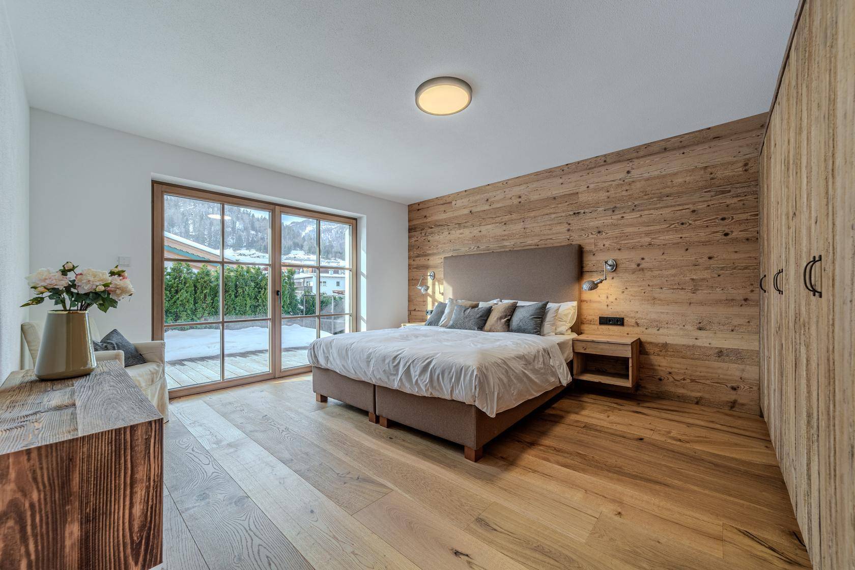 Helles Schlafzimmer mit Holzwand, Einbauschränken und Zugang zum Außenbereich.