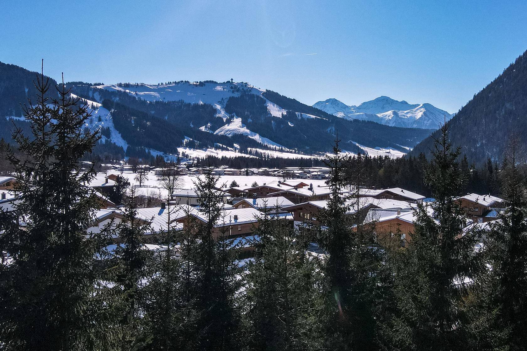 Winterlicher Panoramablick auf ein verschneites Dorf in einem Tal mit schneebedeckten Bergen.