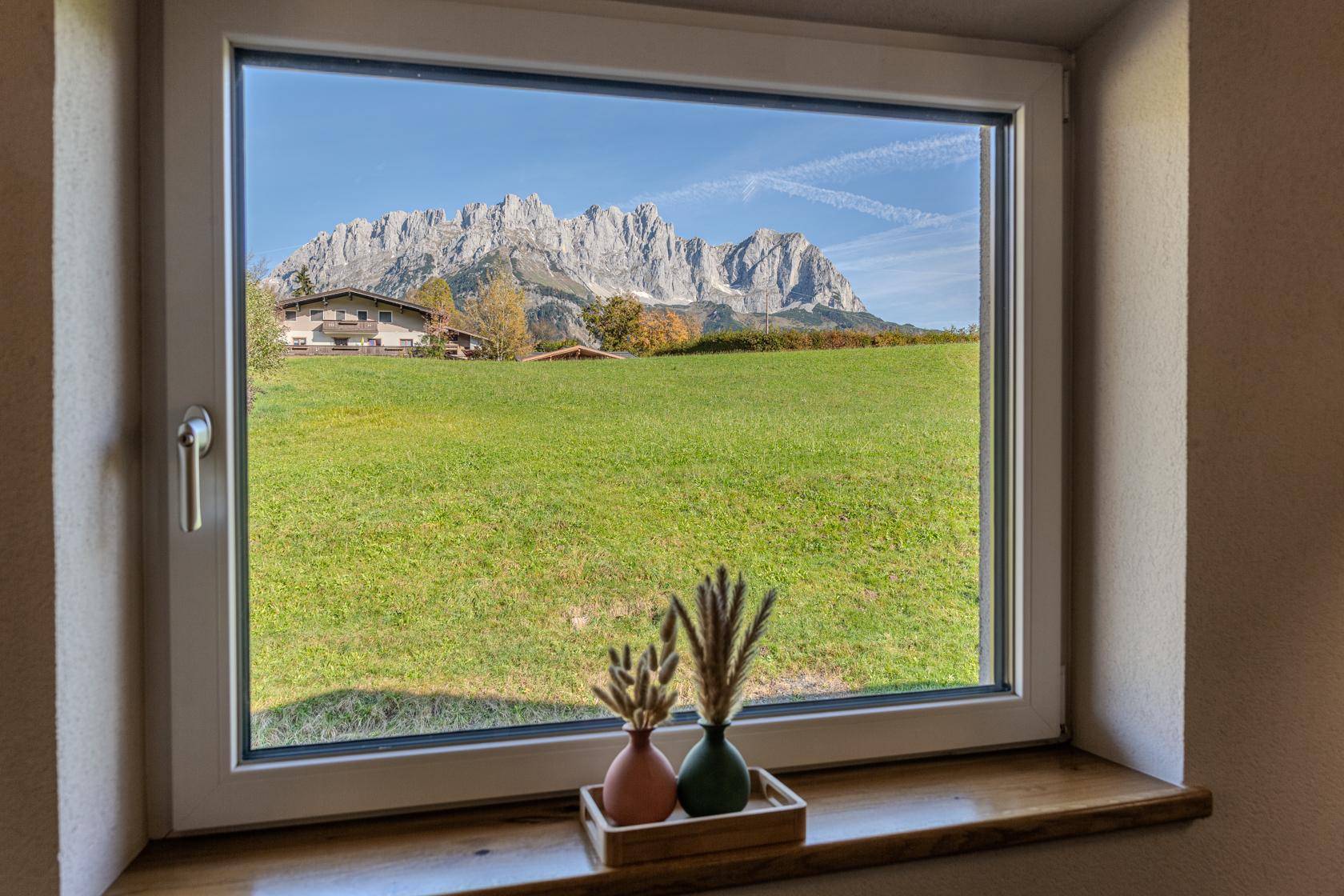 Fensterblick auf grüne Wiesen und die imposante Bergwelt unter strahlend blauem Himmel.