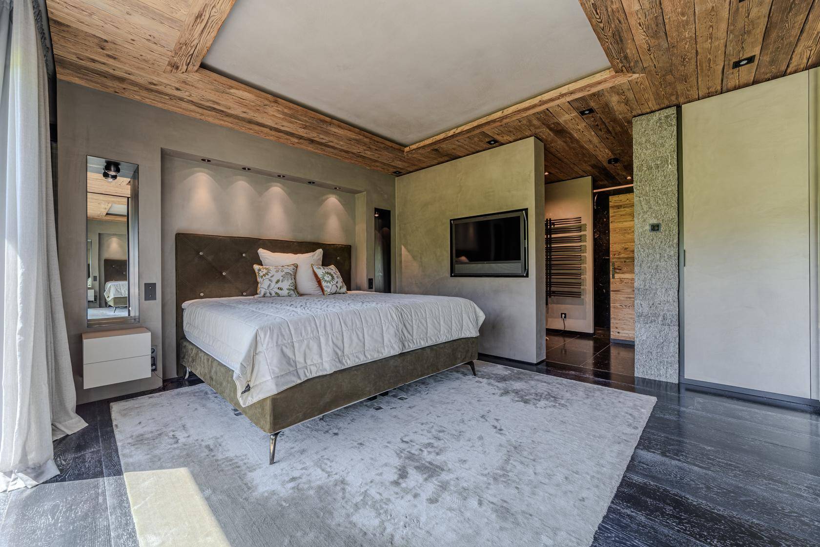 Modernes Schlafzimmer mit Holzakzenten, dunklem Boden und integriertem TV-Bereich.