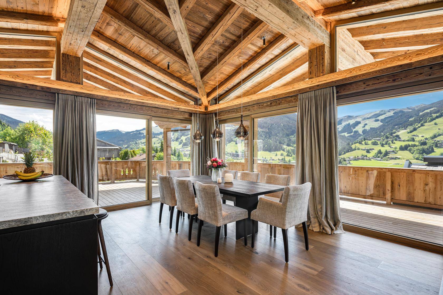 Heller Essbereich mit Holzbalkendecke, großem Esstisch und Panoramablick auf die Berge.