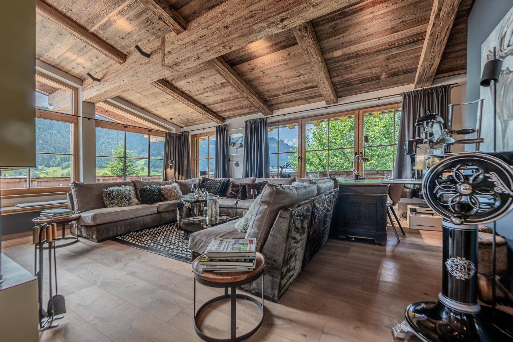 Gemütlicher Wohnbereich mit großem Sofa, Holzbalken und weitem Blick auf die umliegende Berglandschaft.
