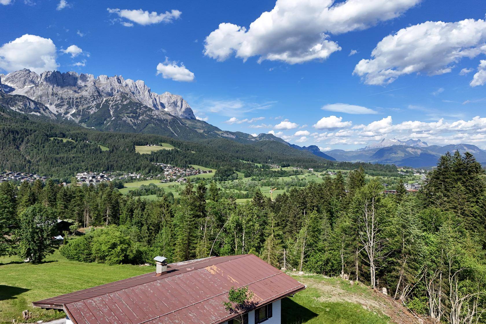 Haus mit rotem Dach und weitem Blick über grüne Wälder und Felder bis zu den imposanten Bergen.