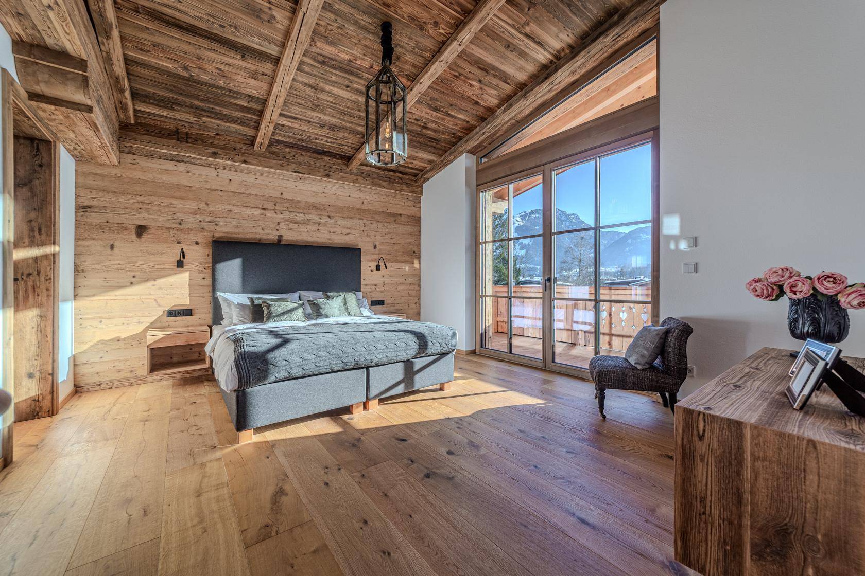Großes Schlafzimmer mit Holzbalkendecke, Holzwänden und Balkonzugang mit Bergblick.