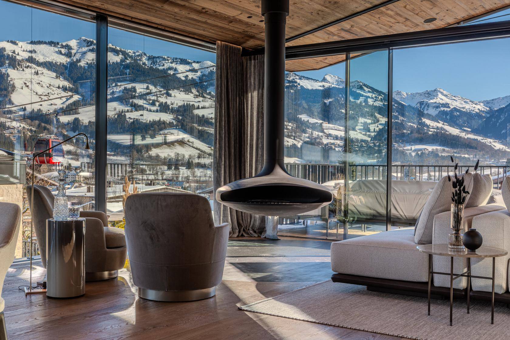 Helles Wohnzimmer mit modernem Kamin, bequemen Sesseln und atemberaubendem Blick auf die verschneiten Berge.