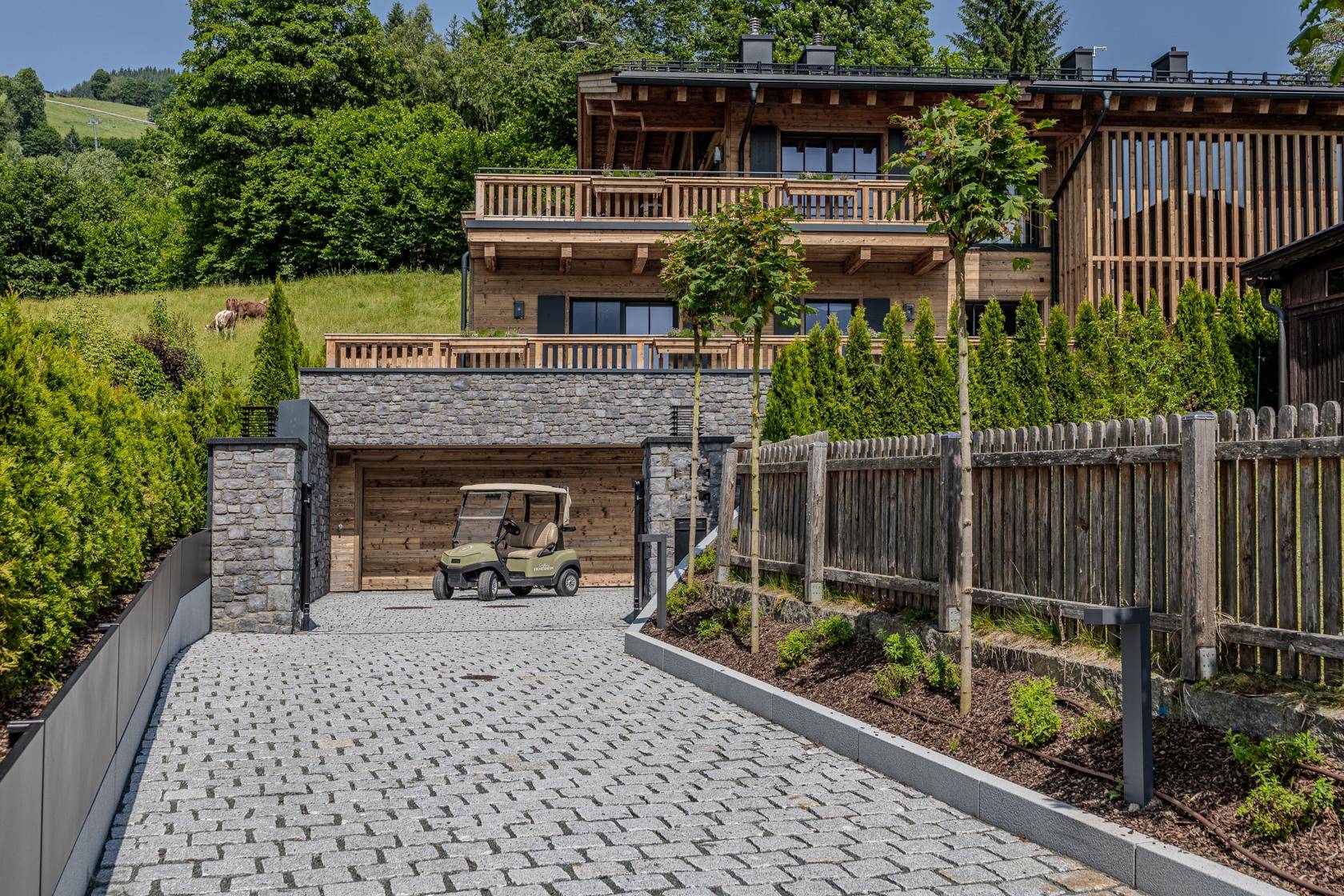 Zufahrt aus Kopfsteinpflaster führt zu einem Garagenbereich mit Golfwagen und dem Haupthaus im alpinen Stil.