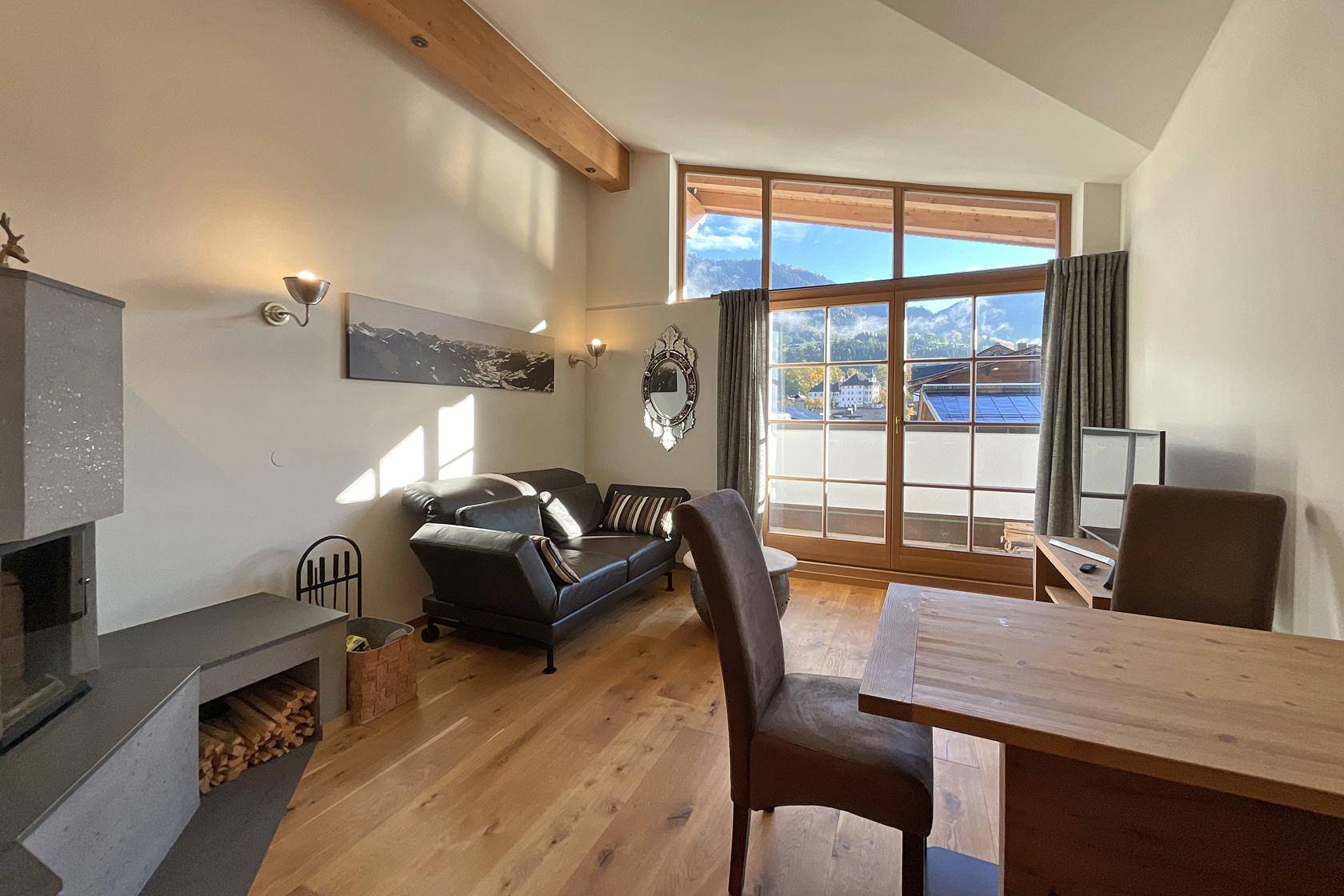 Heller Wohnbereich mit Kamin, bequemer Couch und großen Fenstern mit Bergblick.