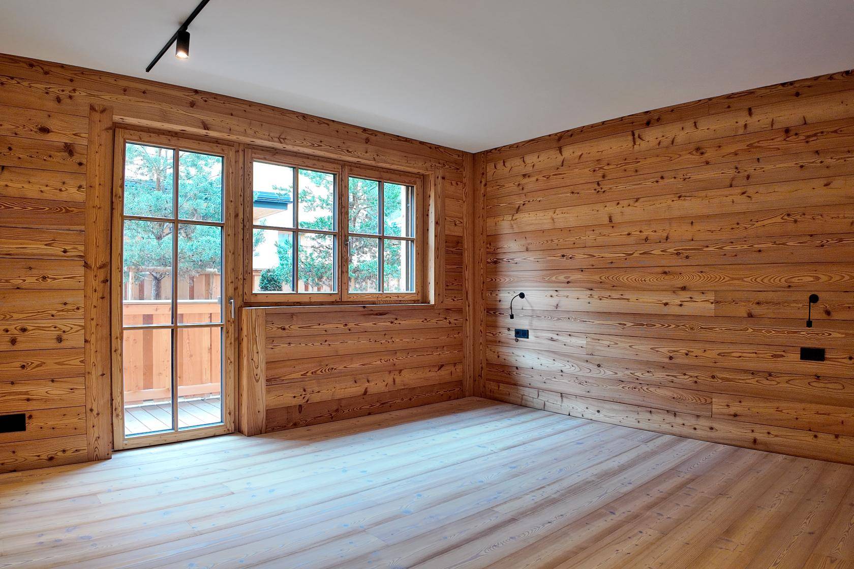 Leerer Raum mit Holzwänden, Holzboden und großen Fenstern, bereit für individuelle Gestaltung.