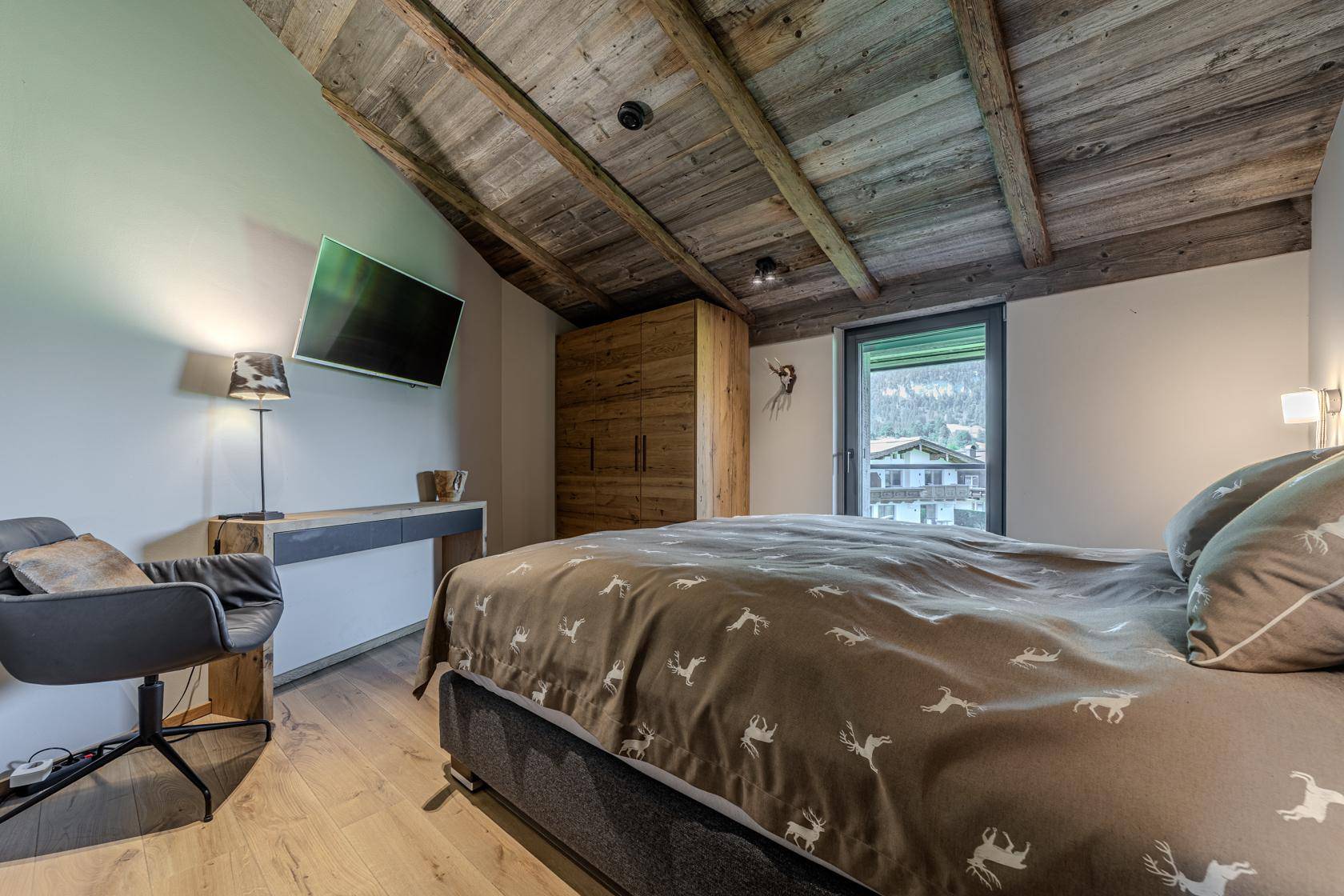 Schlafzimmer mit Holzboden, integriertem Schrank und Schreibtisch, unter einer rustikalen Holzbalkendecke.