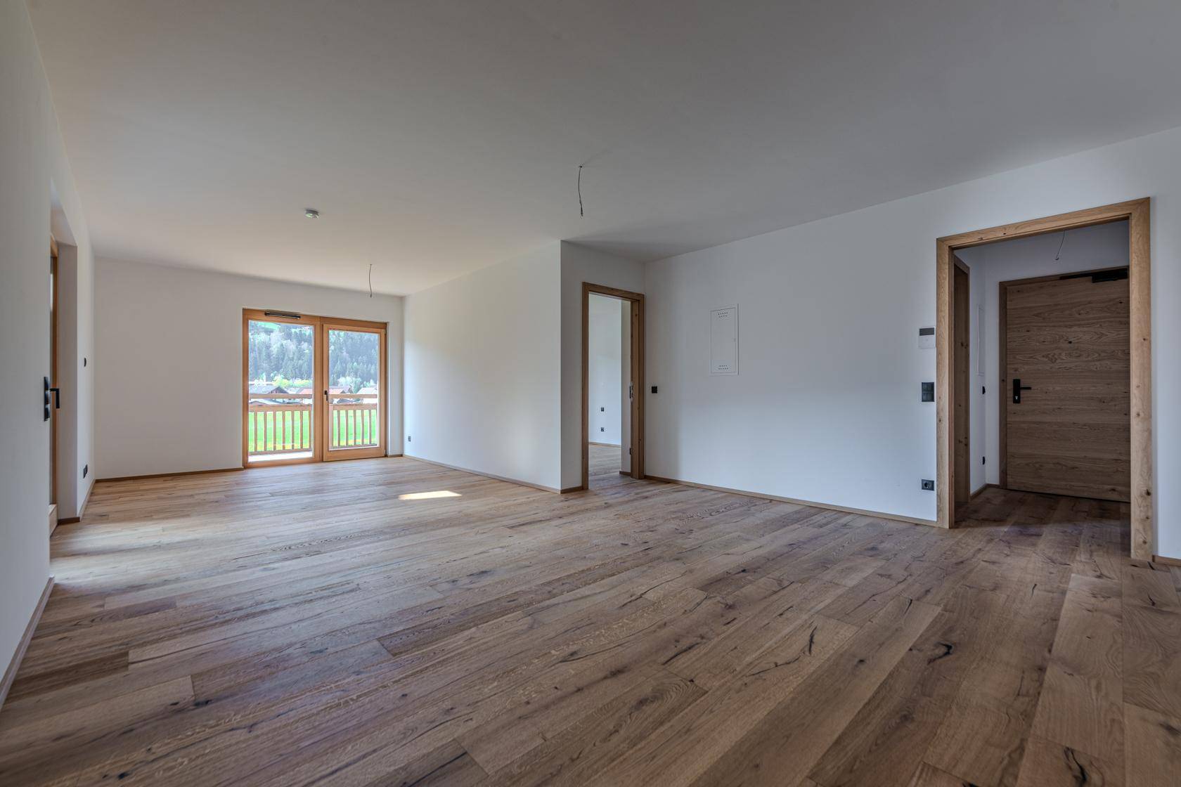 Helles, unmöbliertes Zimmer mit Holzboden und Balkonzugang, bietet einen schönen Blick auf die Berge.