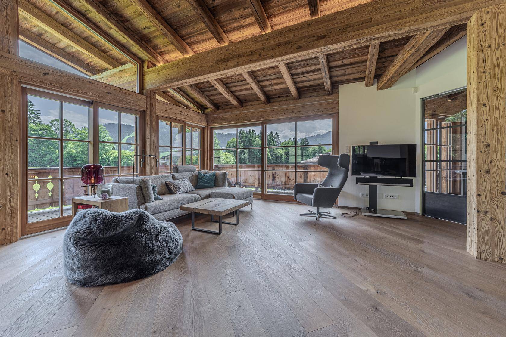 Lichtdurchflutetes Wohnzimmer mit gemütlicher Sitzecke, Holzbalkendecke und Panoramablick.