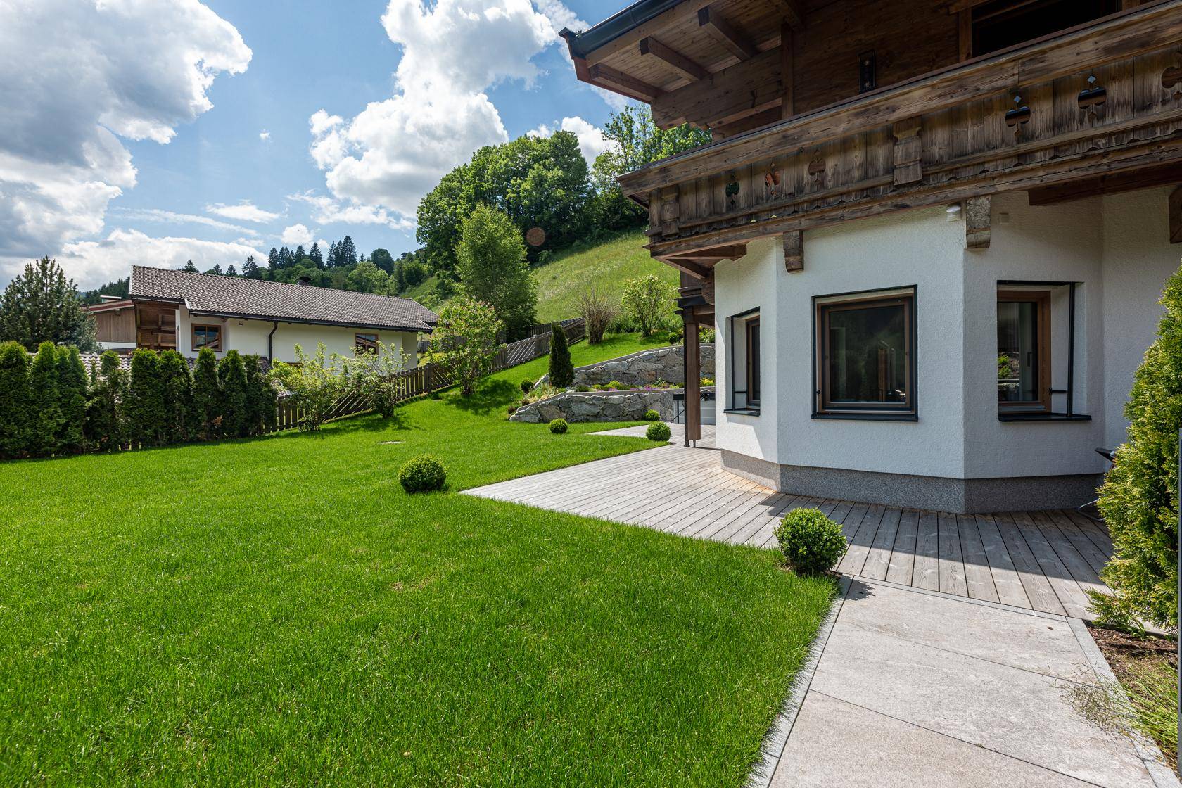 Gepflegter Garten mit Rasenfläche und Holzterrasse vor der modernen Hausfassade.