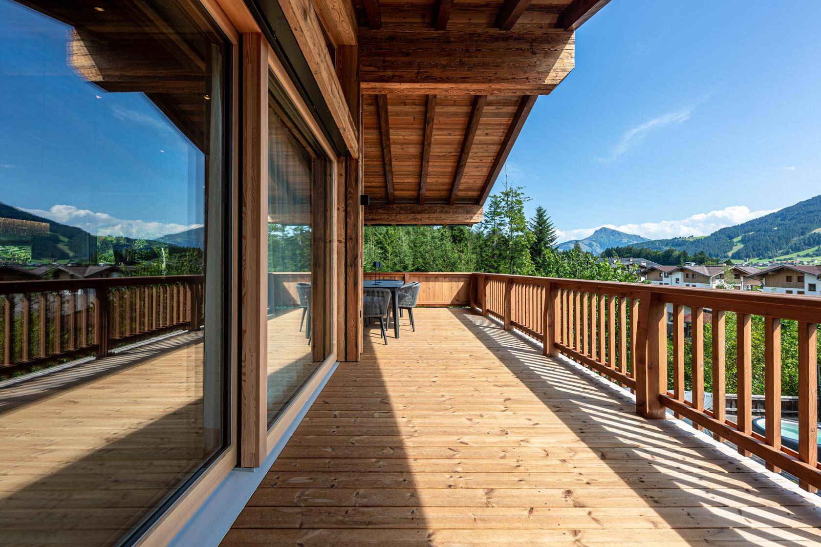 Großer Holzbalkon mit Sitzgelegenheiten und Panoramablick auf die Berge.