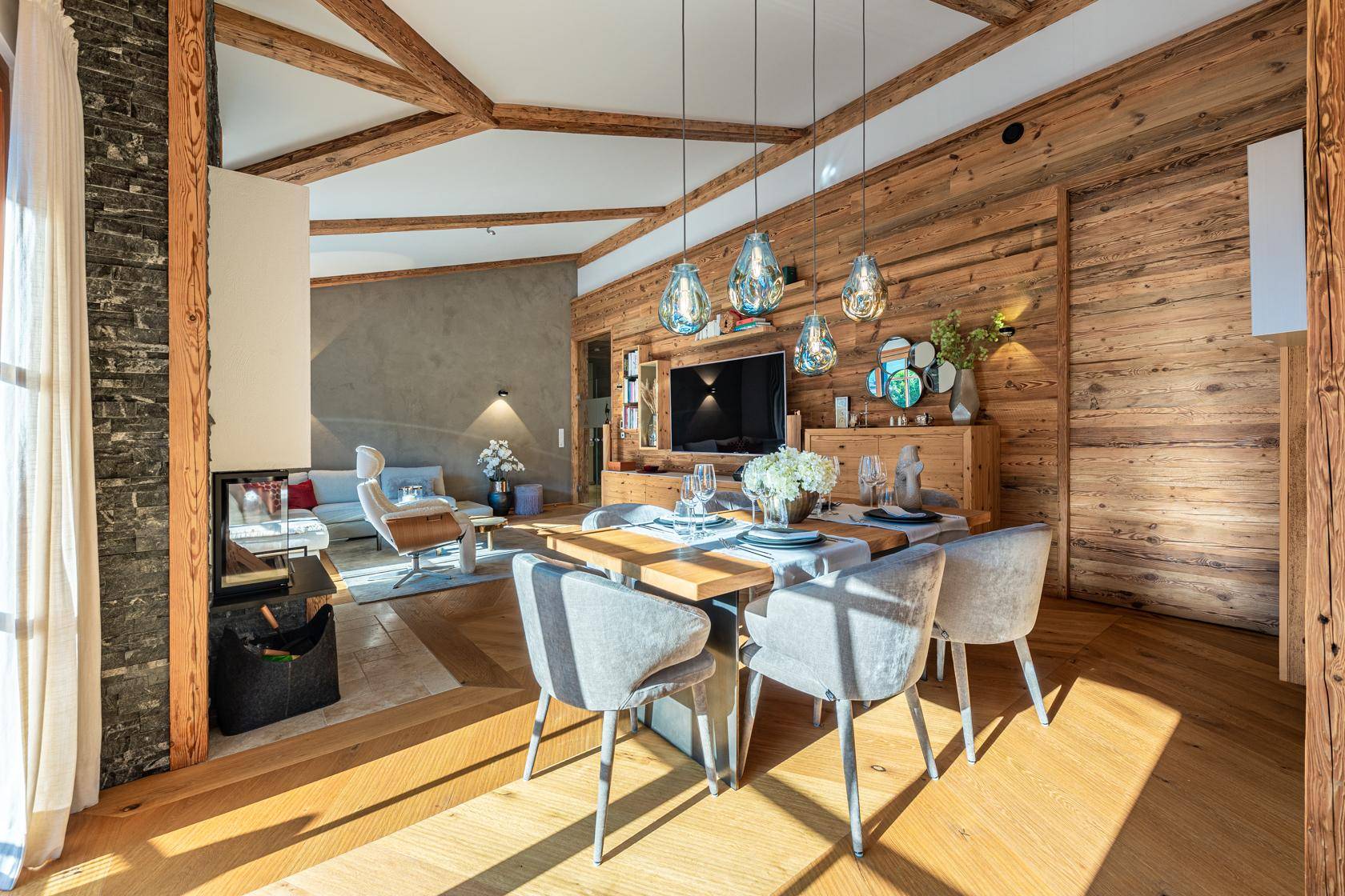 Gemütlicher Essbereich mit Holzwänden, modernen Hängelampen und Blick ins Wohnzimmer.