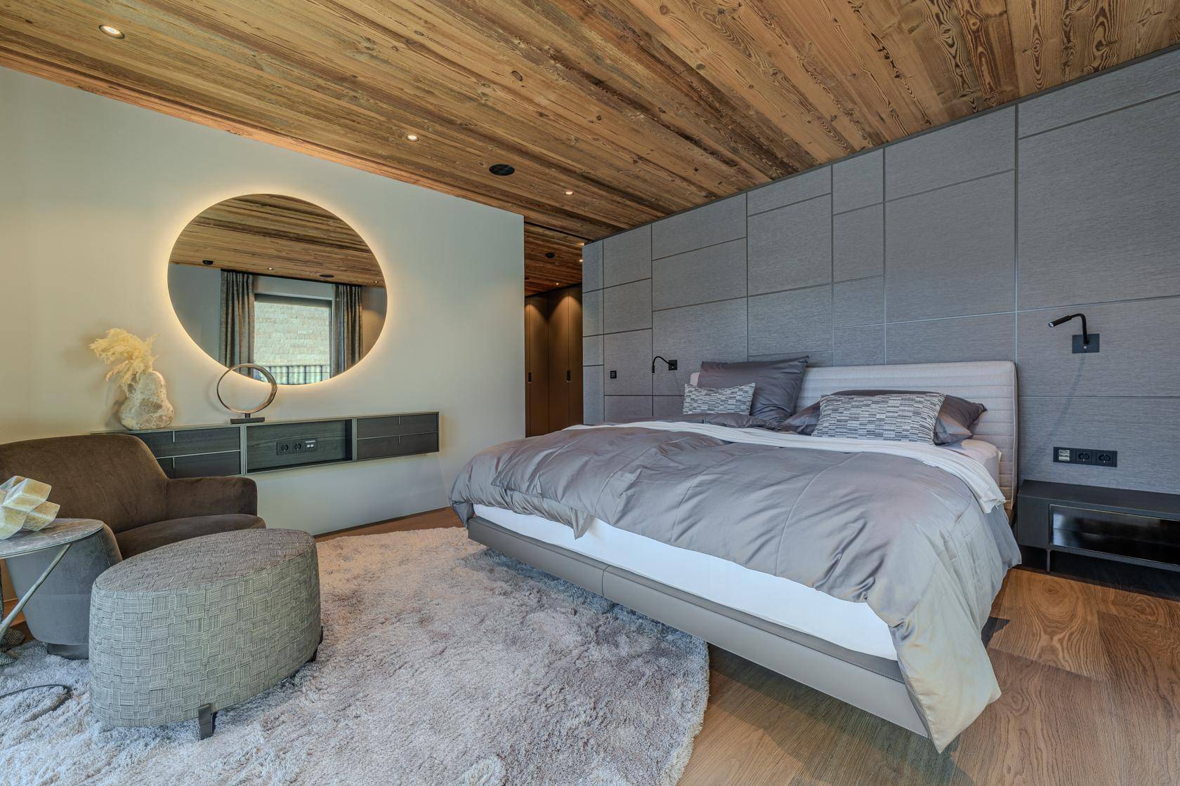 Modernes Schlafzimmer mit Holzbalkendecke, großem Bett und runder Spiegelleuchte.
