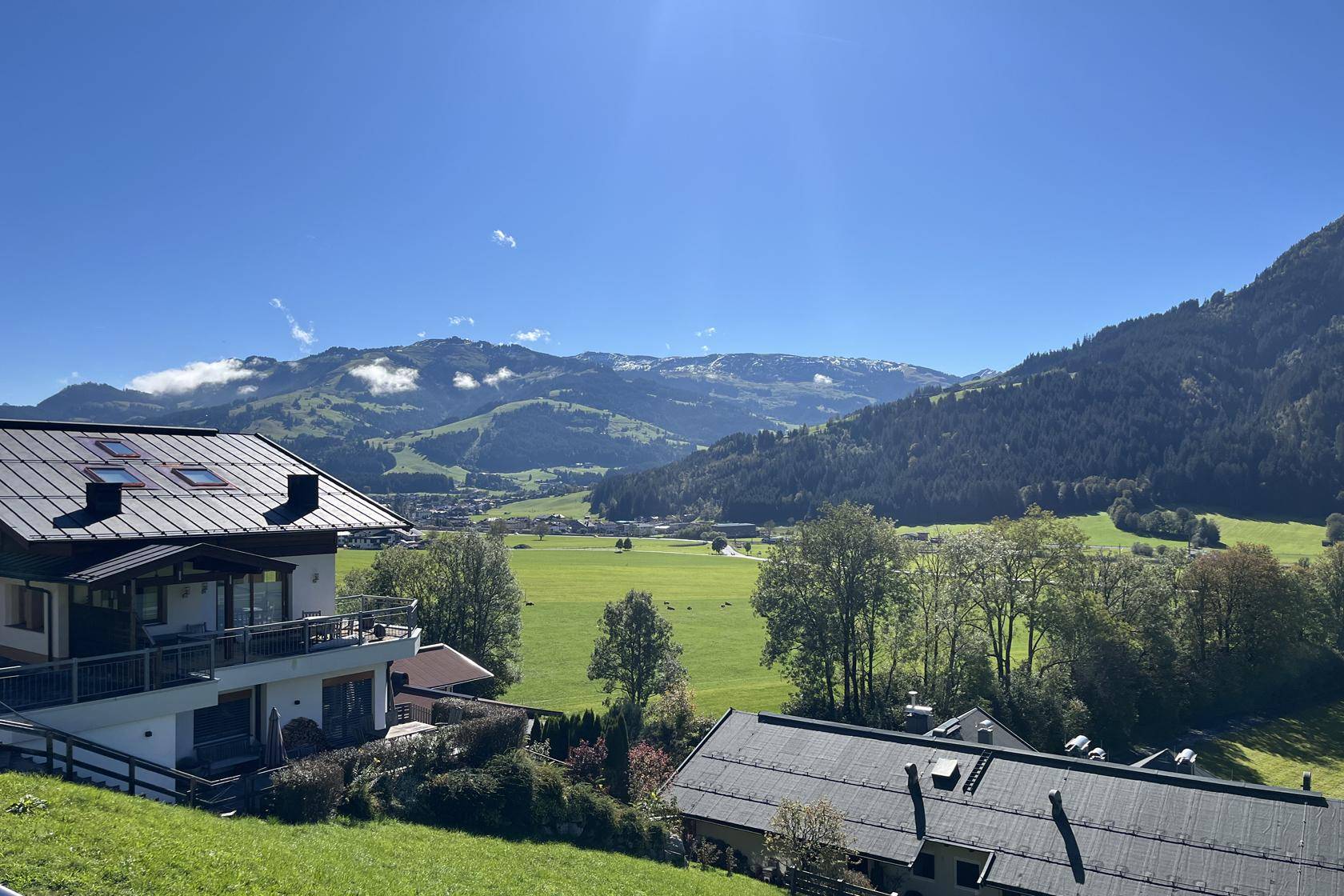 Panoramablick auf die umliegende Berglandschaft und weite grüne Wiesen von einem sonnigen Standort.